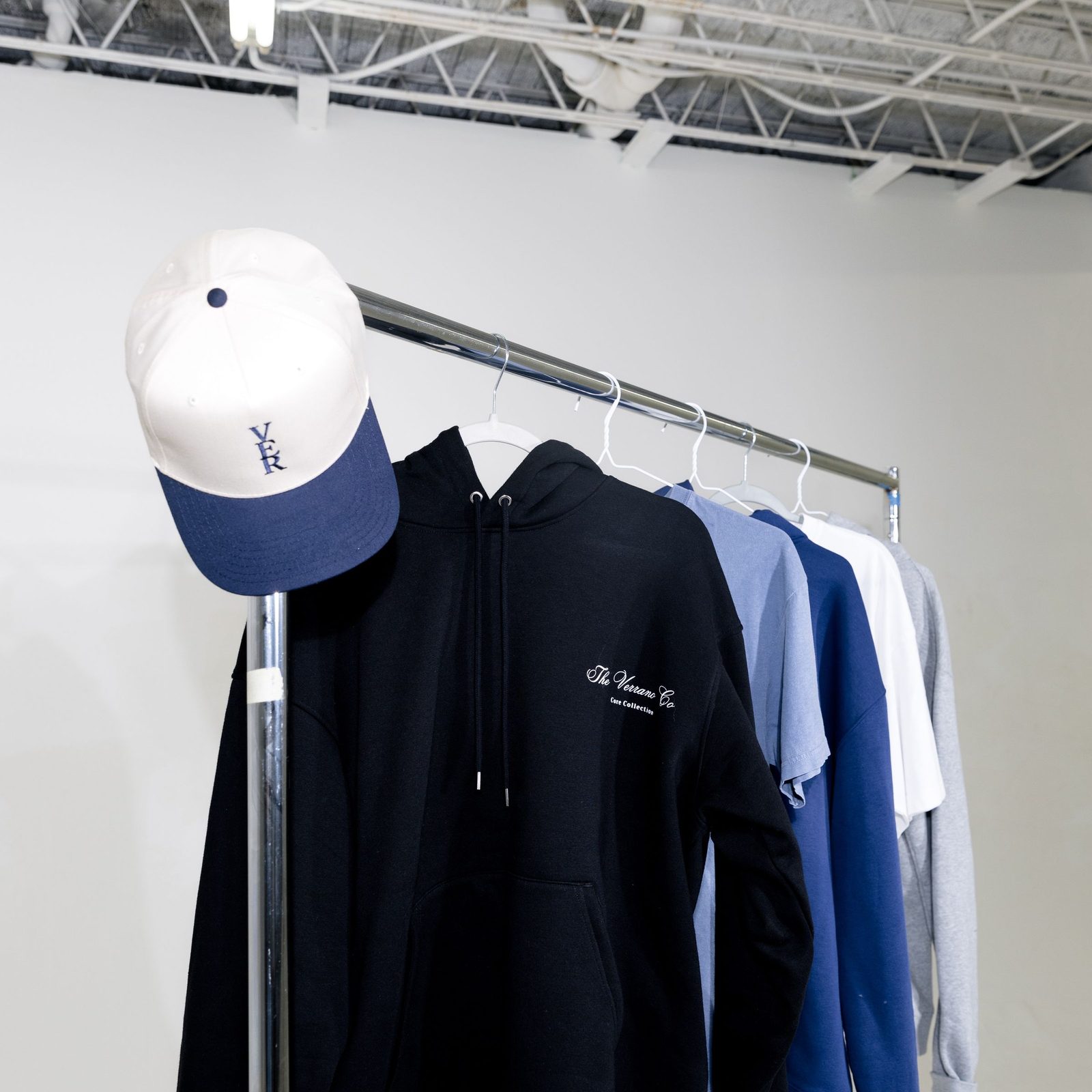 A rack of branded hoodies and shirts beside an embroidered cap